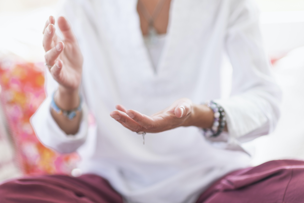 Mindful woman sitting in lotus position, meditating, performing respect gesture with her hands. Spiritual awakening.