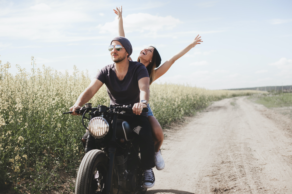 Young romantic couple in a field on a motorcycle. Love, freedom, togetherness concept. Happy guy and girl travel on a motorbike